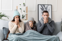 woman, child, and man sitting on couch all blowing their noses