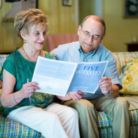 older couple sitting on couch reading a Five Wishes paphlet